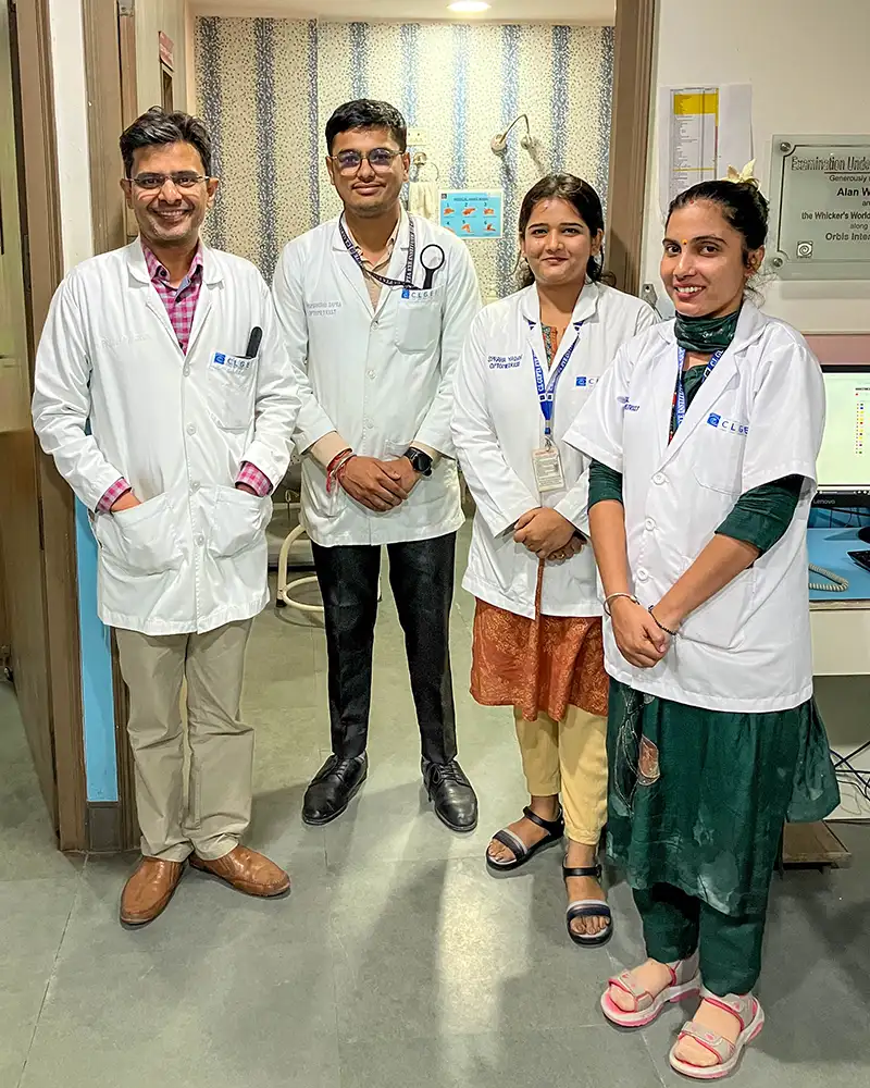 Four health workers wearing medical coats pose for a photo at a clinic.