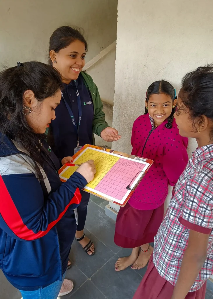 Two women talk to two young girls in school uniforms. One of the women holds a clipboard.